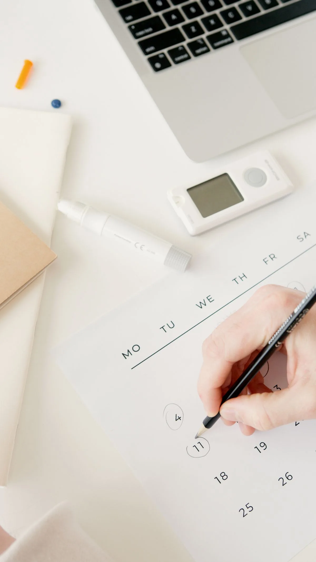 A hand marks a date on a calendar beside a laptop and medical equipment